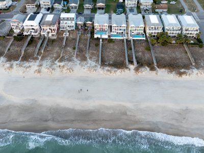 Top-down sunrise view of Kure Beach with beachfront houses and advancing waves, highlighting climate change concerns in North Carolina.
